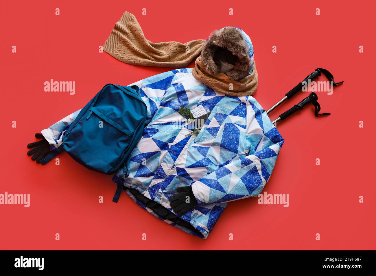 Rucksack mit Pufferjacke und Skistöcken auf rotem Hintergrund Stockfoto