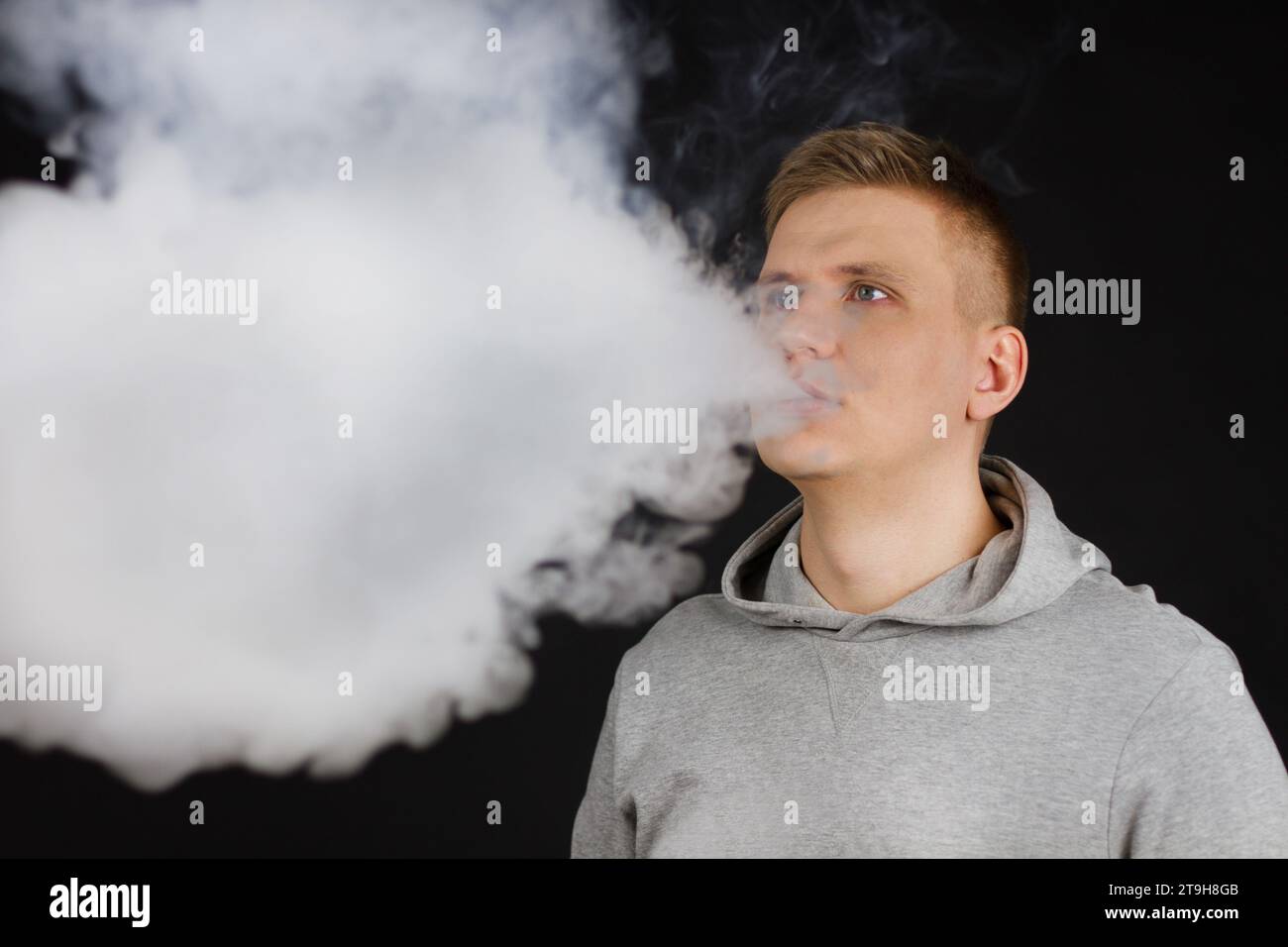 Männer in Kapuze dampfen und entfalten eine Wolke aus Dampf. Selektiver Fokus Stockfoto