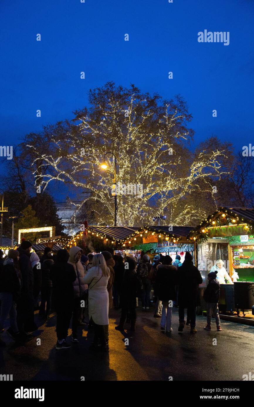 Baum geschmückt mit wunderschönen Weihnachtslichtern auf dem geschäftigen Weihnachtsmarkt (Wiener Christkindlmarkt) im Winter in der Nacht, Rathause, Wien, Österreich Stockfoto