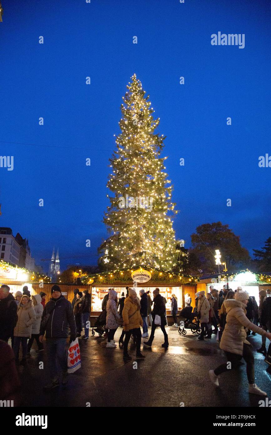 Baum geschmückt mit wunderschönen Weihnachtslichtern auf dem geschäftigen Weihnachtsmarkt (Wiener Christkindlmarkt) im Winter in der Nacht, Rathause, Wien, Österreich Stockfoto