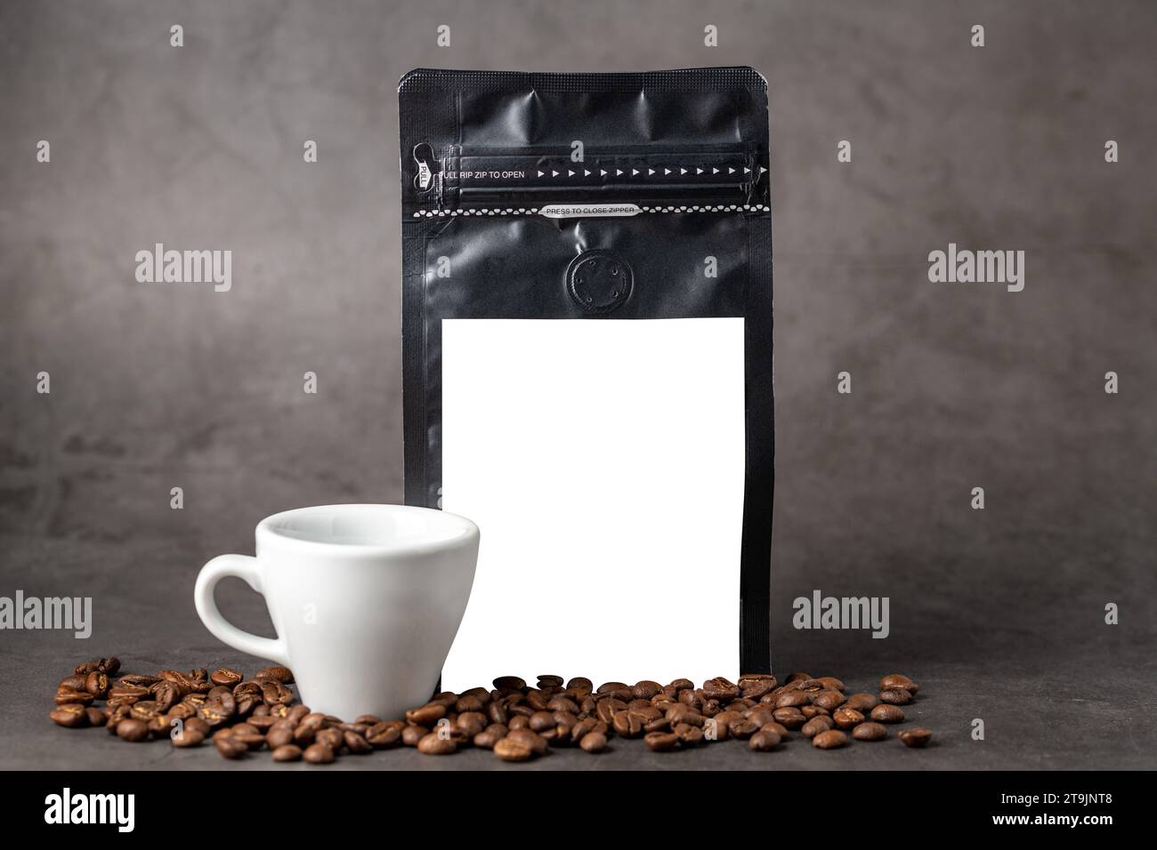 Verpackungsbeutel aus schwarzer Kaffeefolie und Kaffeetasse mit leerem weißem Etikett auf Steintisch Stockfoto