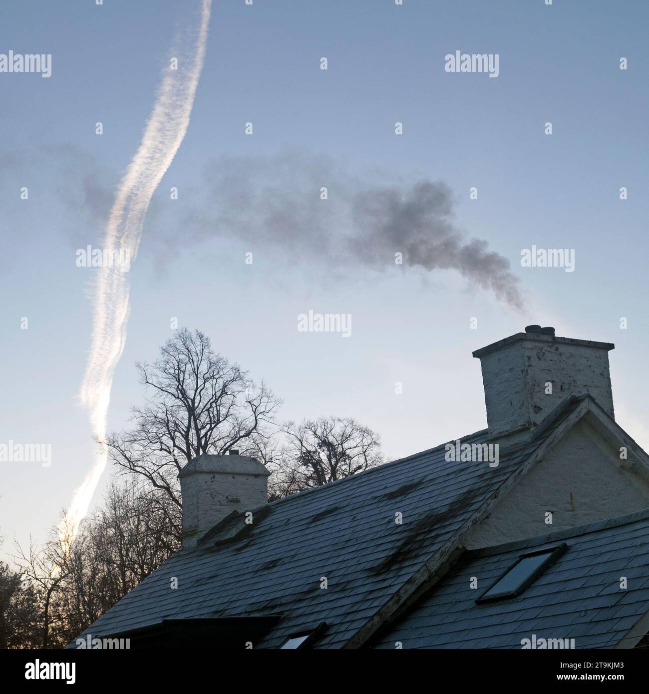 Rauch steigt aus einem Landhaus Haus im Winter und Dampfspur aus dem Flugzeug im Winter Morgen blauer Himmel ländliches Wales UK KATHY DEWITT Stockfoto