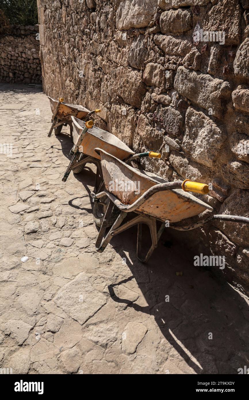 Drei Schubkarren, die auf eine Steinmauer in Spanien gelehnt sind Stockfoto