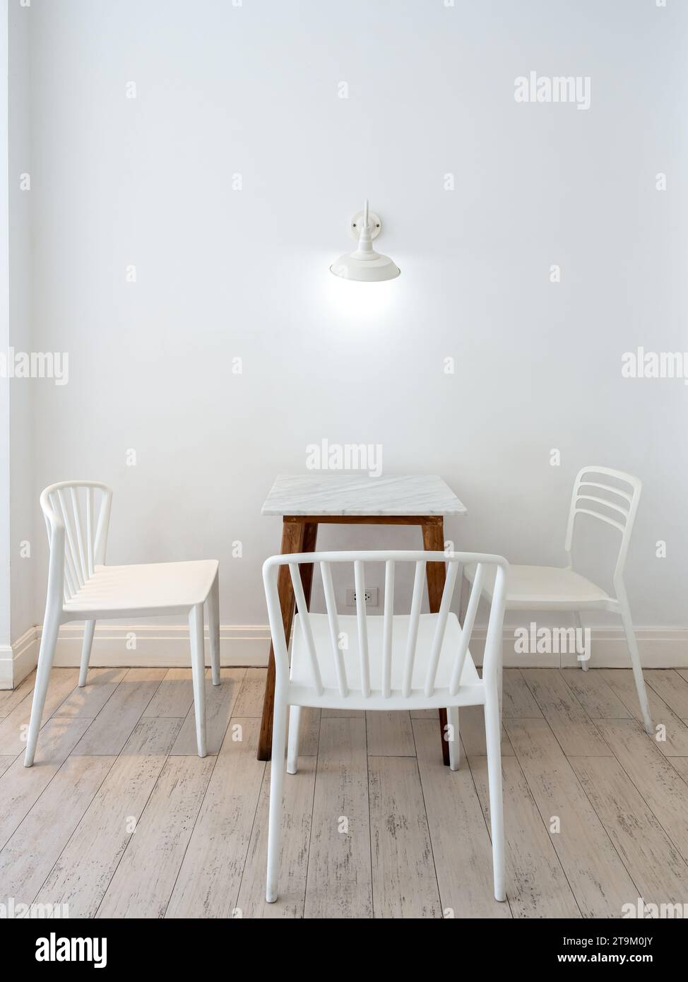 Vintage-Lampen hängen an der weißen Wand über dem leeren Esstisch mit Marmortisch mit Holzbeinen und drei Stühlen, minimalistischer Wohnstil Stockfoto