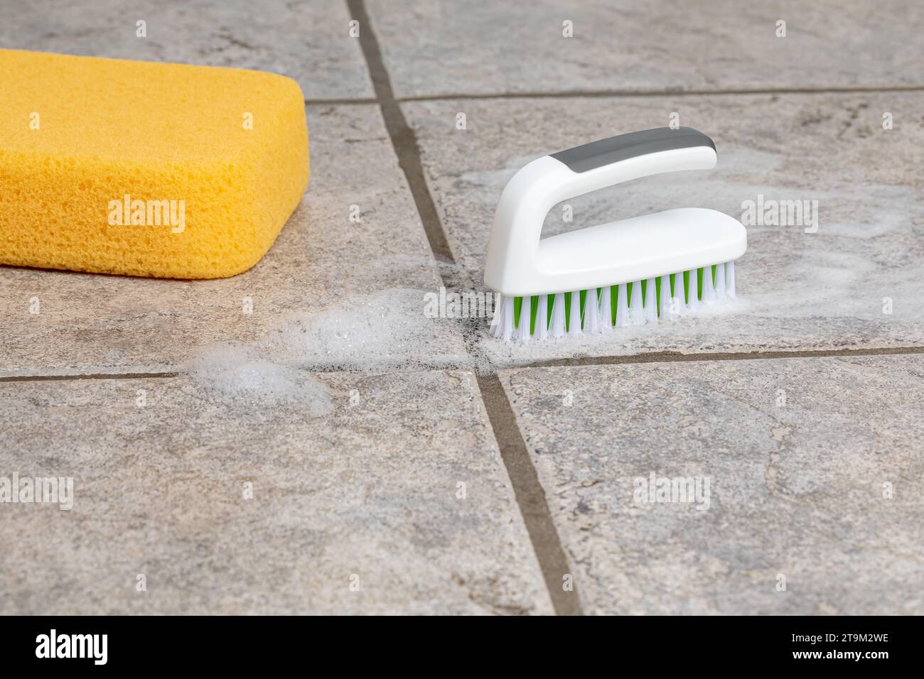 Reinigung von Keramikfliesenböden mit Scheuerbürste und Schwamm. Haushalt, Hausarbeit und Bodenpflegekonzept. Stockfoto