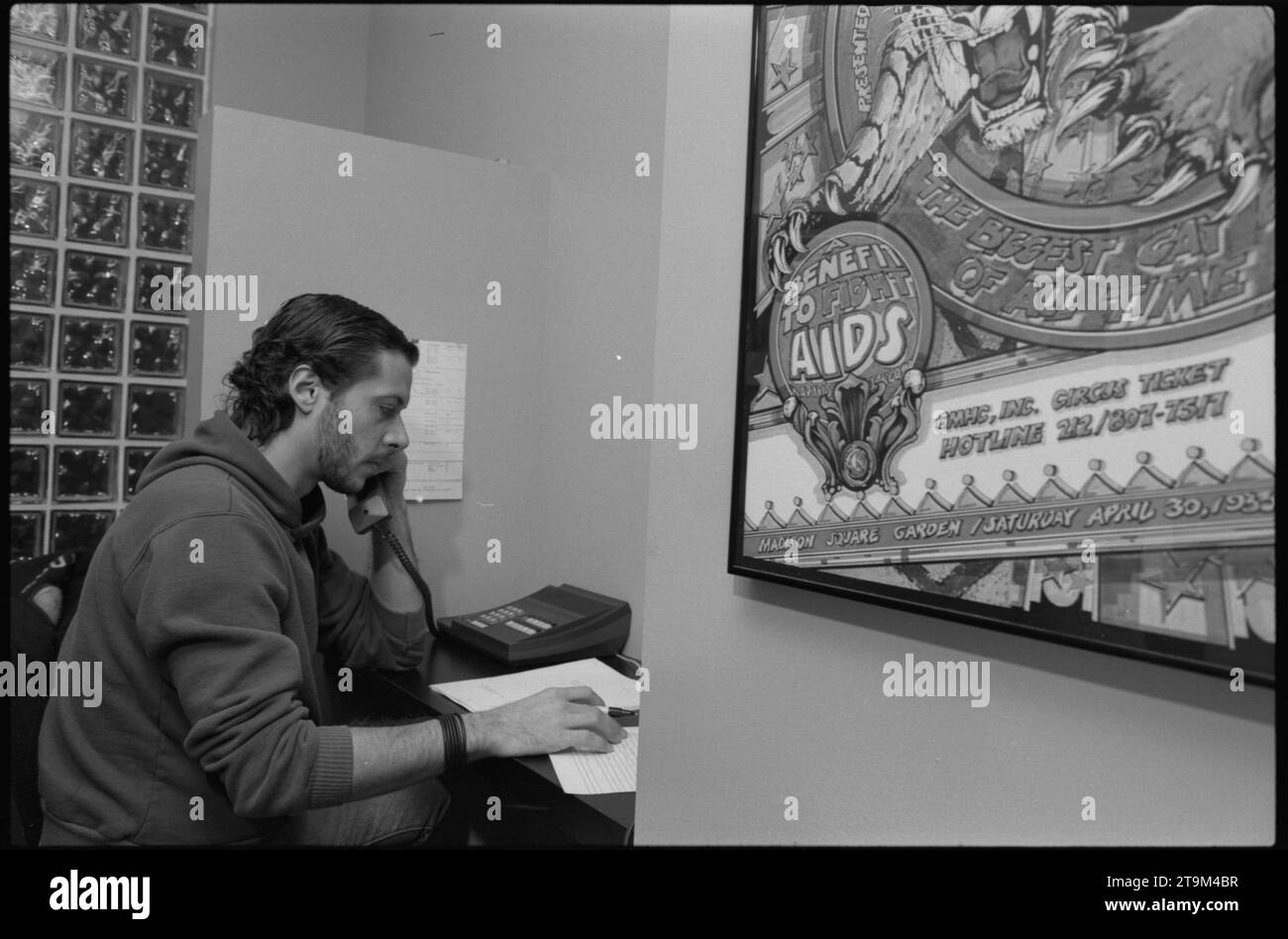 Ein unbekannter Mann, der an einem Schreibtisch neben einem Plakat sitzt, das für eine Aktion zur Bekämpfung von AIDS wirbt, geht an einer AIDS-Hotline, New York, 14.11.1984, ans Telefon. (Foto: William Scott Thode/US News & World Report Magazine Collection) Stockfoto