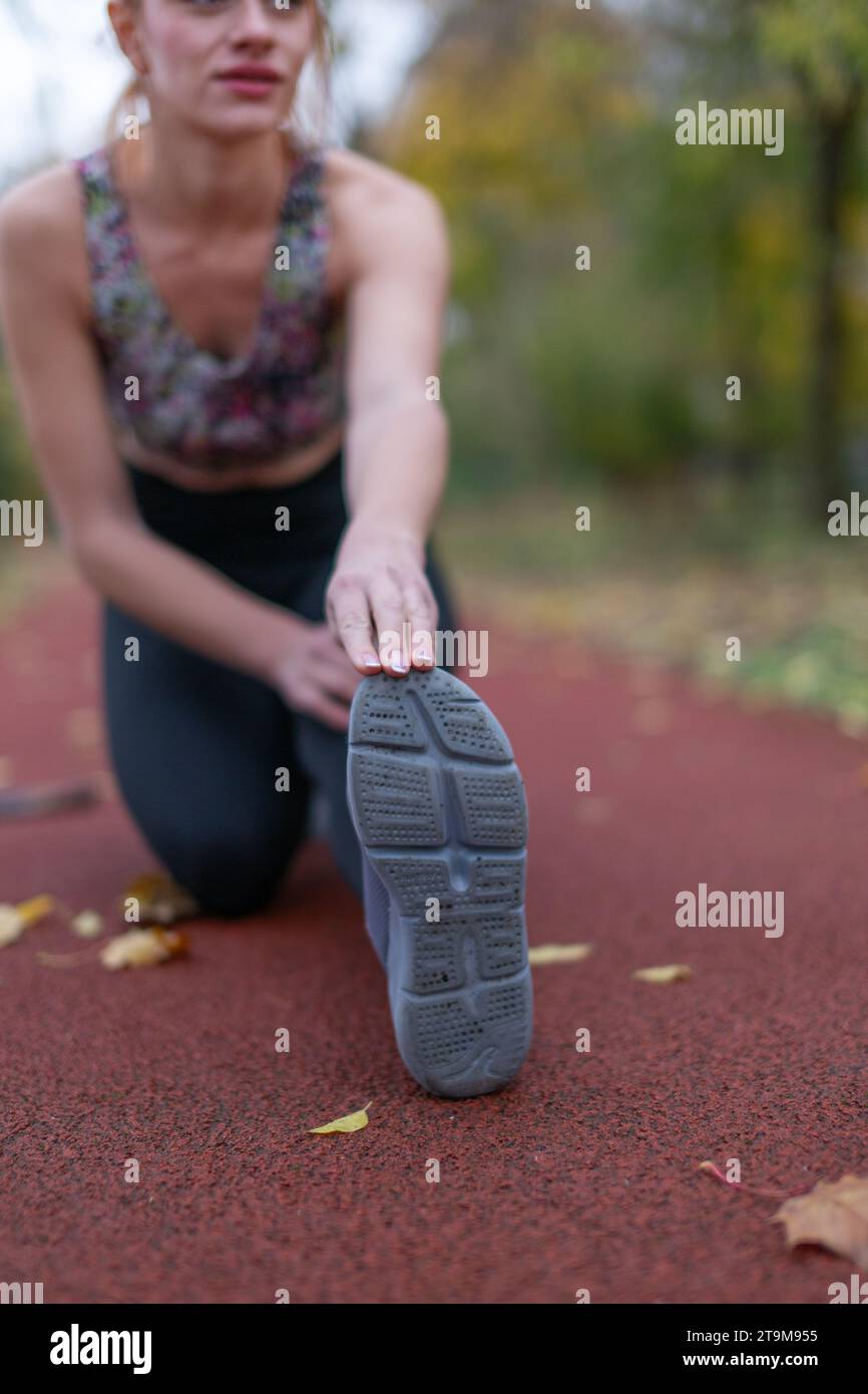 Junge Frau, die sich aufwärmt, bevor sie im Herbst auf der Strecke läuft, Tiefen des Feldes Stockfoto
