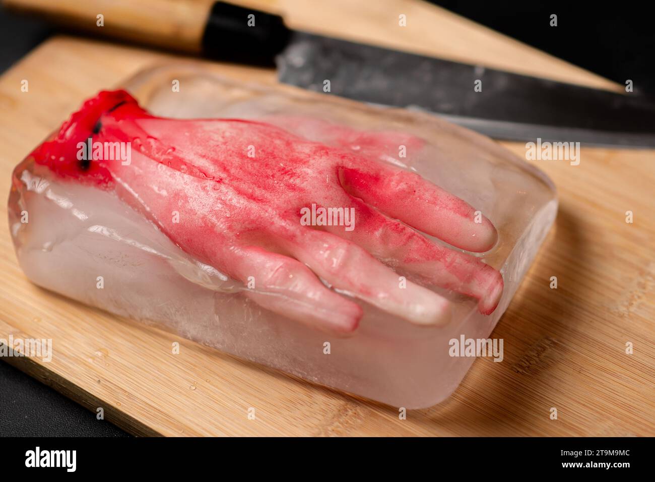 Ice Terror: Ein Horror-Konzept, bei dem ein menschliches Modell in einem Stück Eis auf einem hölzernen Schneidebrett eingefroren ist, was ein knochenkühlendes und beunruhigendes C erzeugt Stockfoto