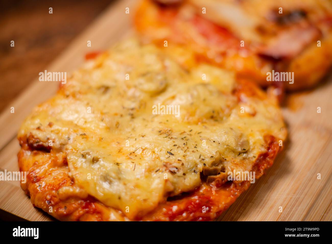 Kulinarische Köstlichkeiten: Ein Duo aus kleinen, selbst gebackenen Pizzen, jede mit aromatischem Schinken und geschmolzenem Käse, präsentiert auf einem hölzernen Schneidebrett Stockfoto