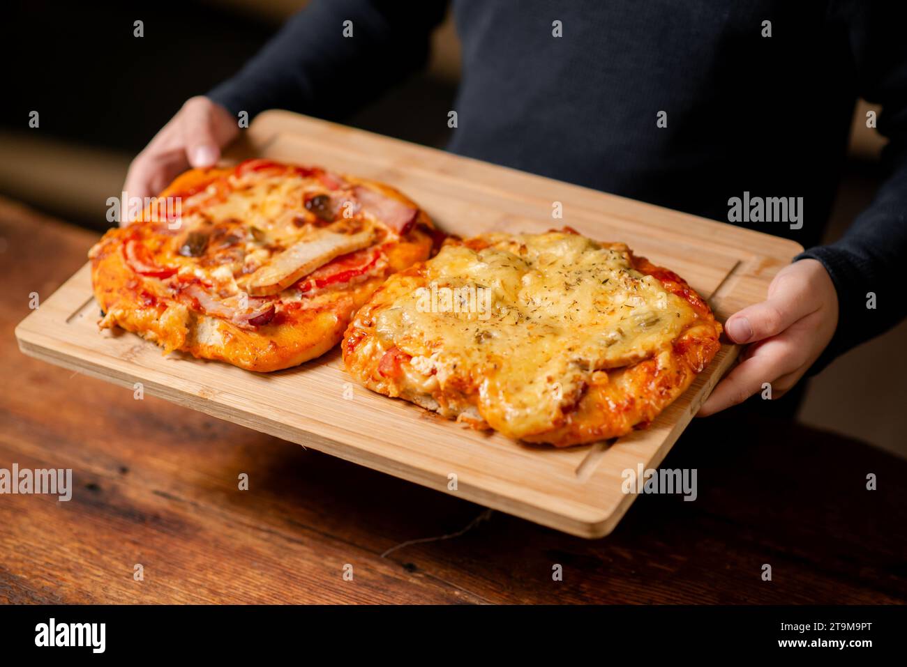 Artisan Pizza Pairing: Ein Duo aus kleinen selbstgemachten Pizzen, die von männlichen Händen auf einer Holzoberfläche gehalten werden Stockfoto