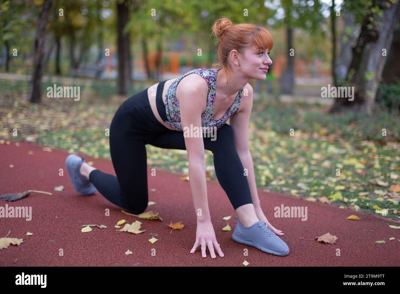 Die junge rothaarige, optimistische weiße Frau in Sportkleidung, die Sprint übt, startet im Herbst auf der Laufstrecke Stockfoto