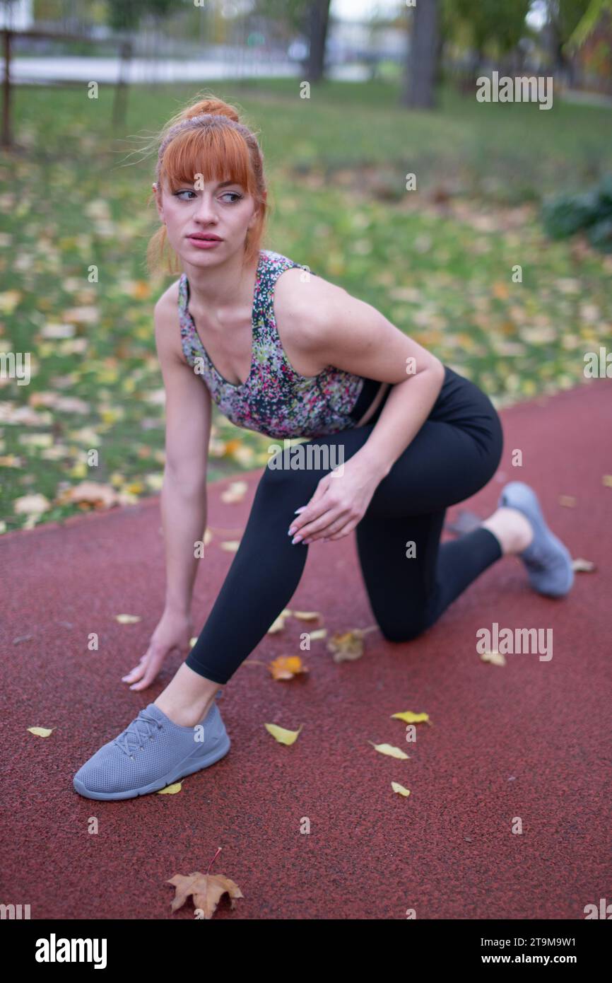 Junge rothaarige Kaukasierin in Sportbekleidung, bevor sie im Herbst auf die Laufbahn startet Stockfoto