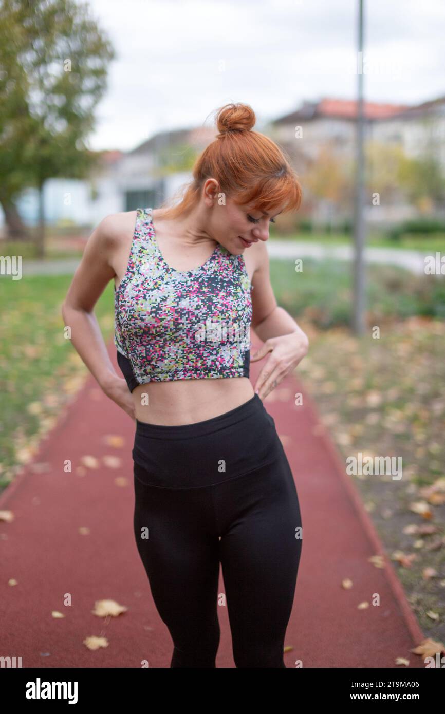 Junge rothaarige Kaukasierin in Sportswear, die im Herbst auf der Laufbahn ihre Form überprüft Stockfoto