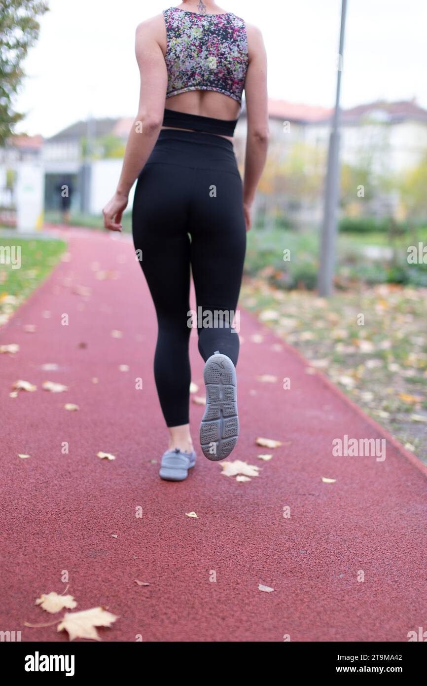 Joggingfrauenkörper in Sportbekleidung auf Laufbahn im Spätherbst-Rückansicht Stockfoto