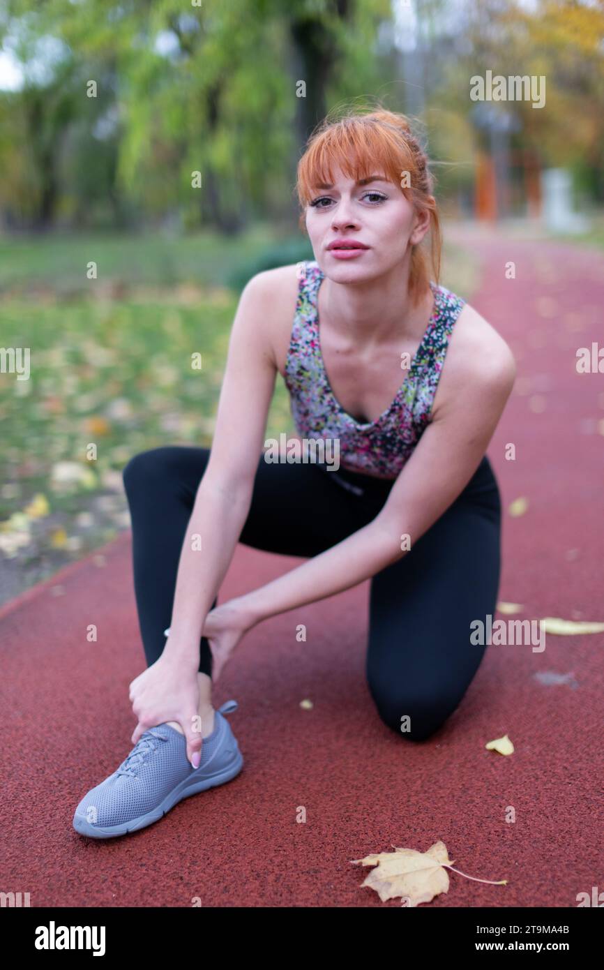Junge rothaarige Kaukasierin in Sportkleidung mit schmerzhafter Knöchelverletzung auf Laufbahn Stockfoto