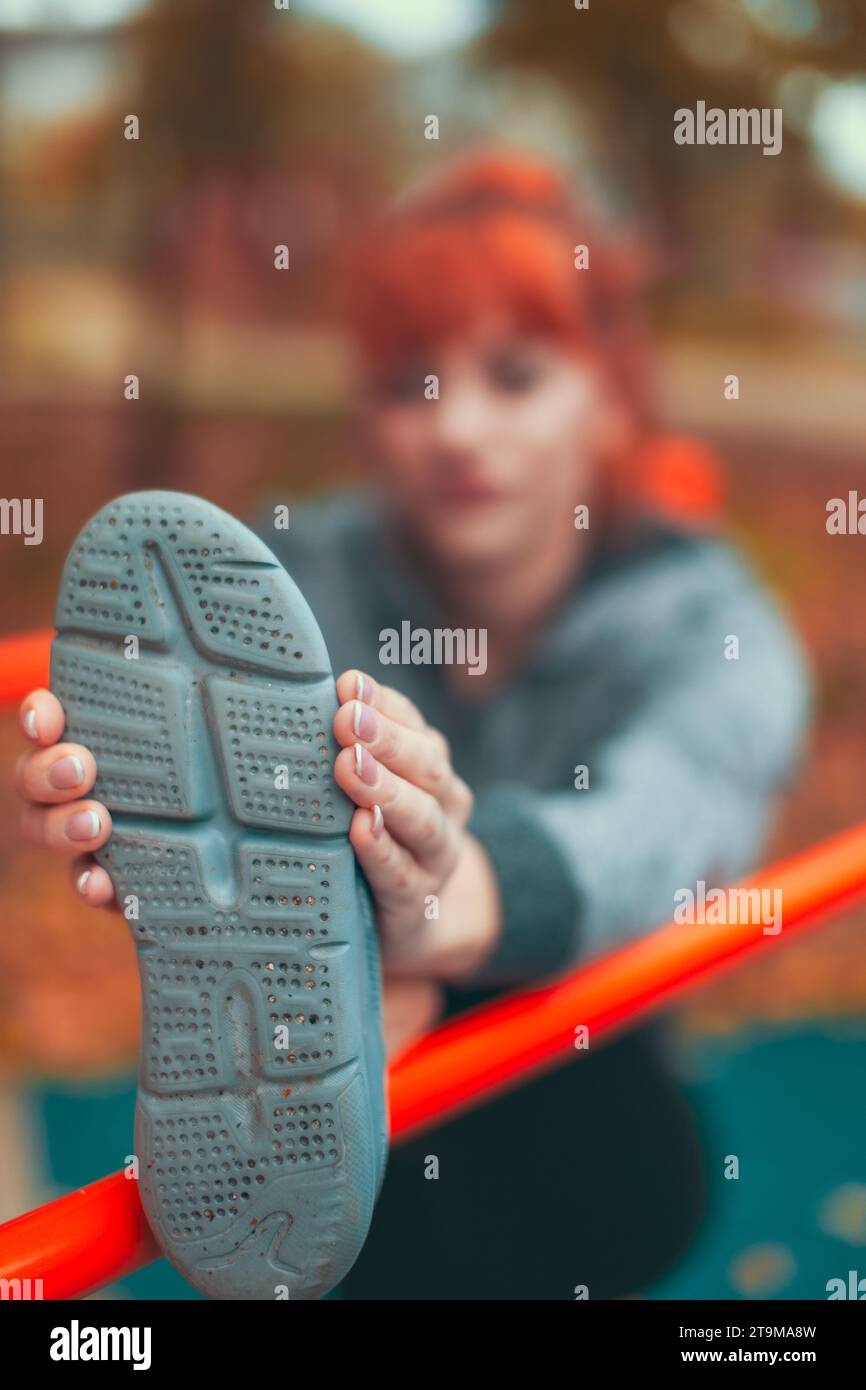 Junge kaukasische Frau, die sich aufwärmt und ihr Bein an der Bar im Park im lebhaften Herbst dehnt, konzentriert euch auf Schuhe Stockfoto