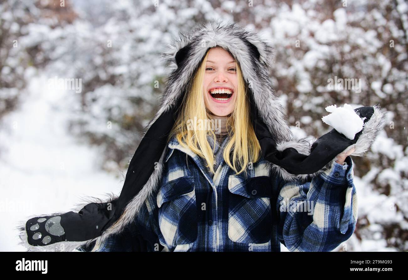 Wintersaison. Glückliches Mädchen, das im Winterpark mit Schnee spielt. Schöne Frau im karierten Mantel, Pelzmütze und Fäustlinge am schneebedeckten Wintertag. Lächelnde Blondine Stockfoto