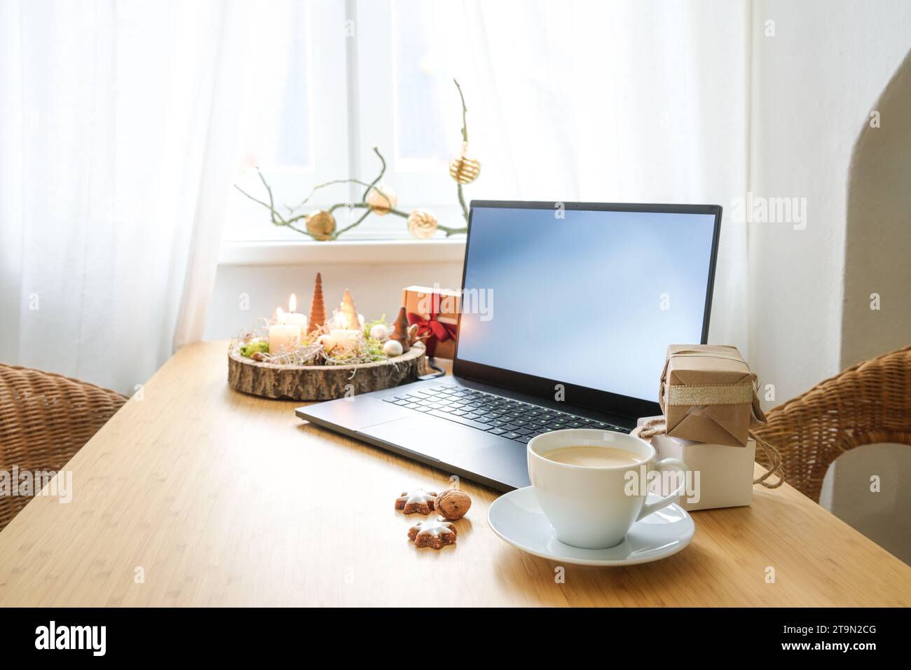 Laptop auf einem Holztisch am Fenster in einem Apartment im Dachgeschoss. Geschenke, Adventskerzen, Weihnachtsdekoration und eine Kaffeetasse. Online-Shopping im Urlaub, Co Stockfoto