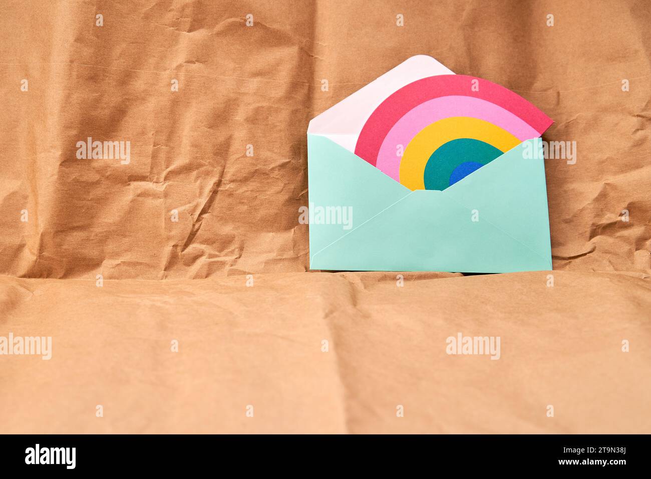 Grüner Umschlag mit einer Karte in Regenbogenform auf einem strukturierten Hintergrund aus Karton. Stockfoto