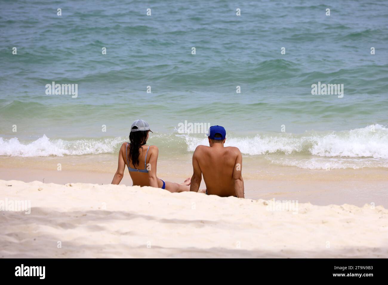 Pärchen sitzen auf einem Sand auf Meeresgrund. Mann und Frau in Bademode zusammen, romantischer Urlaub und Strandurlaub Stockfoto