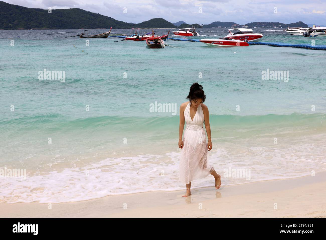 Asiatisches Mädchen in weißem Kleid, das am Sand auf tropischem Strand auf Motorboothintergrund läuft. Urlaub auf Coral Island, Koh Hey Stockfoto