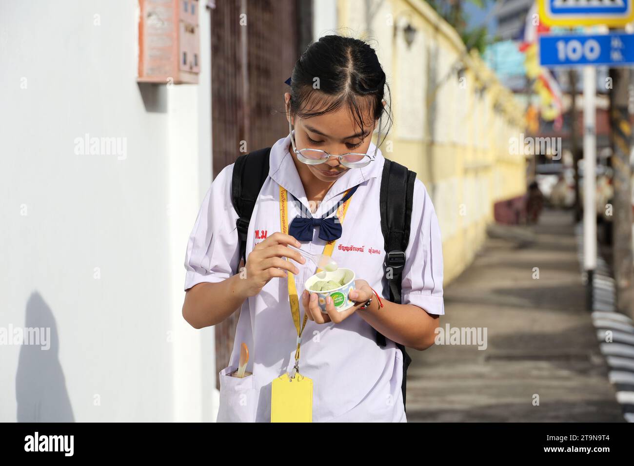 Thai-Mädchen mit Brille isst Eis und läuft die Straße entlang Stockfoto