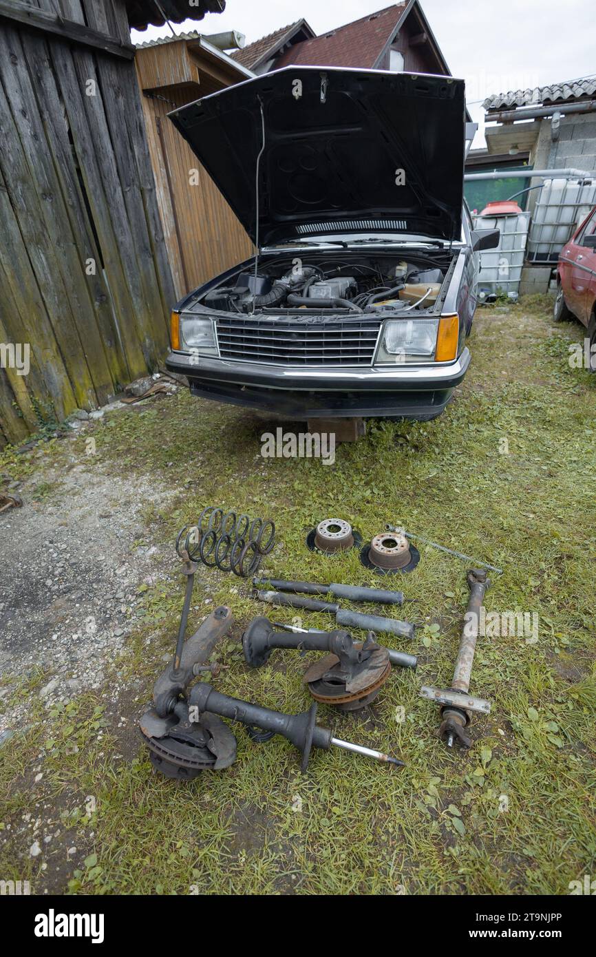 Altes oder vitales Fahrzeug mit ausgebauten Autoteilen wie Stoßdämpfern, Bremsscheiben und Federbeinen, das vor dem Fahrzeug im Gras liegt. Stockfoto