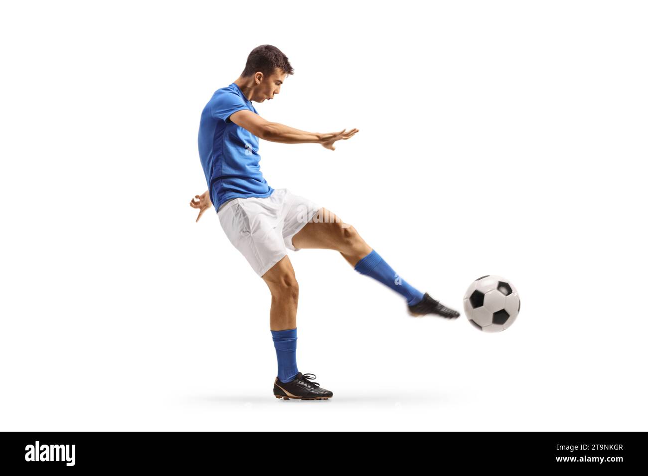 Profilaufnahme eines jungen Fußballspielers in einem blauen Trikot, der einen Ball auf weißem Hintergrund tritt Stockfoto