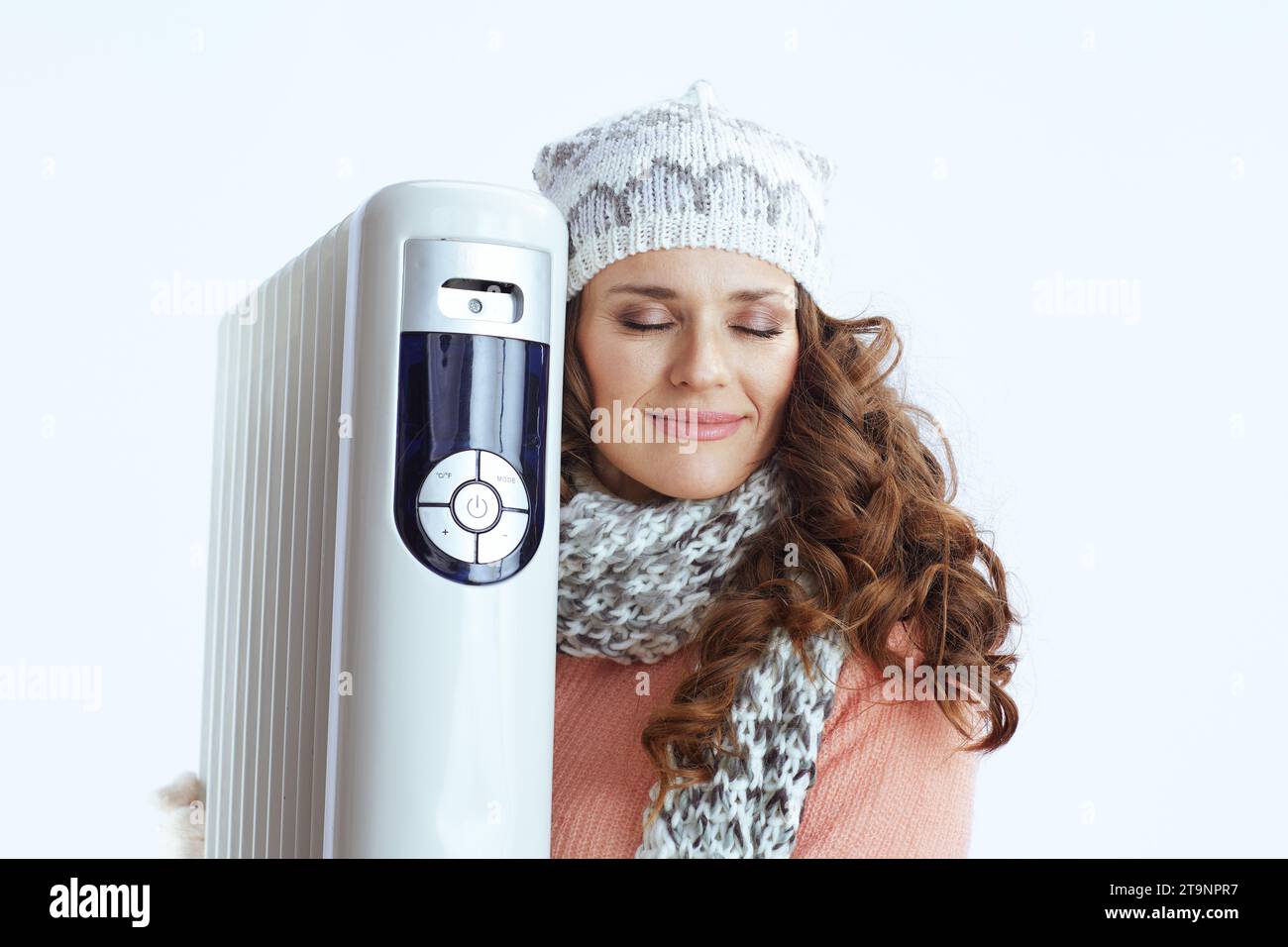 Hallo Winter. Lässige trendige Frau in Pullover, Fäustlingen, Mütze und Schal mit Heizung isoliert auf weiß. Stockfoto