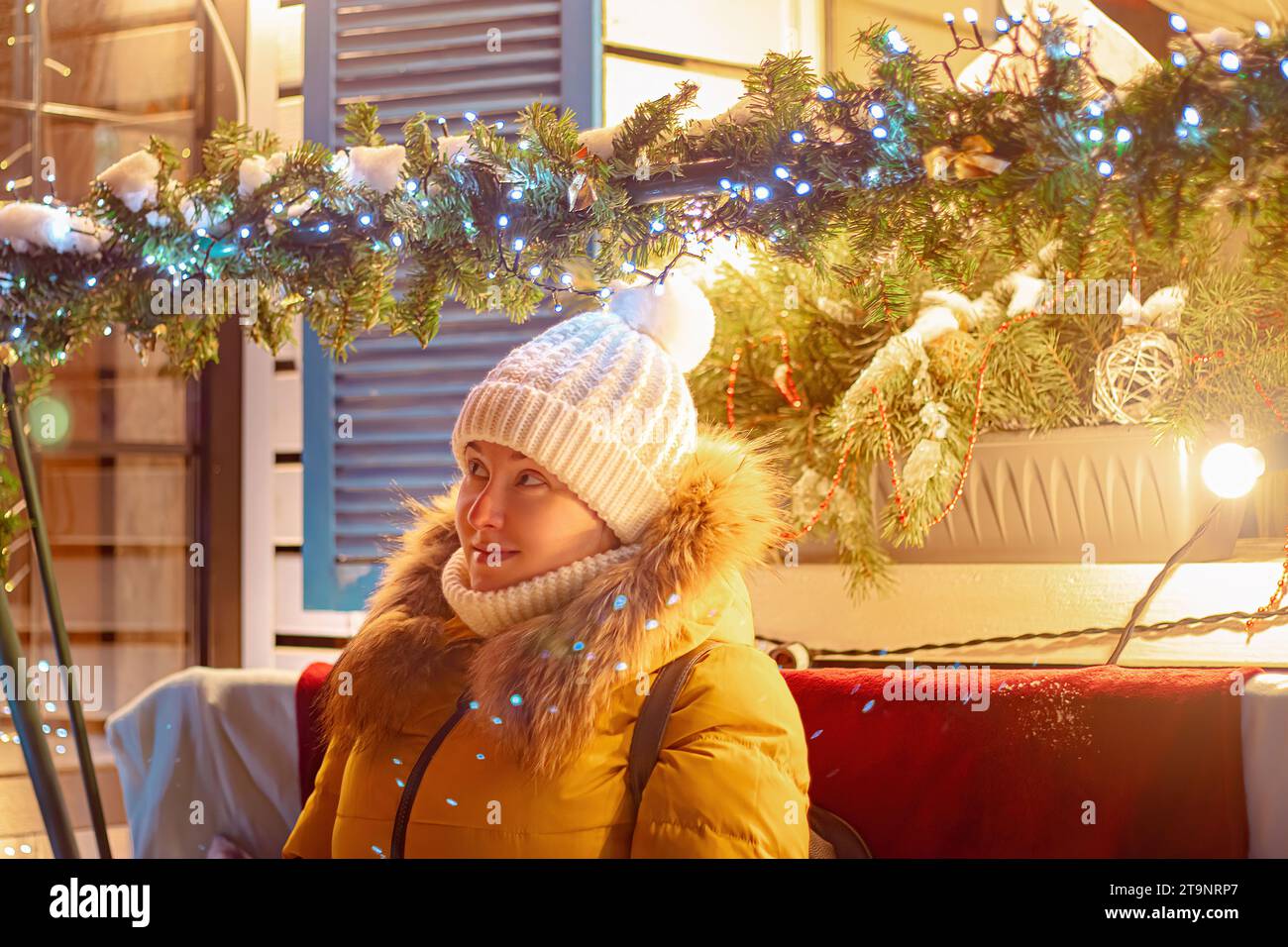 Die junge Touristin in Strickmütze schaut sich festliche Weihnachtsdekorationen an. Weihnachtsmarkt, Nachtbeleuchtung. Stockfoto