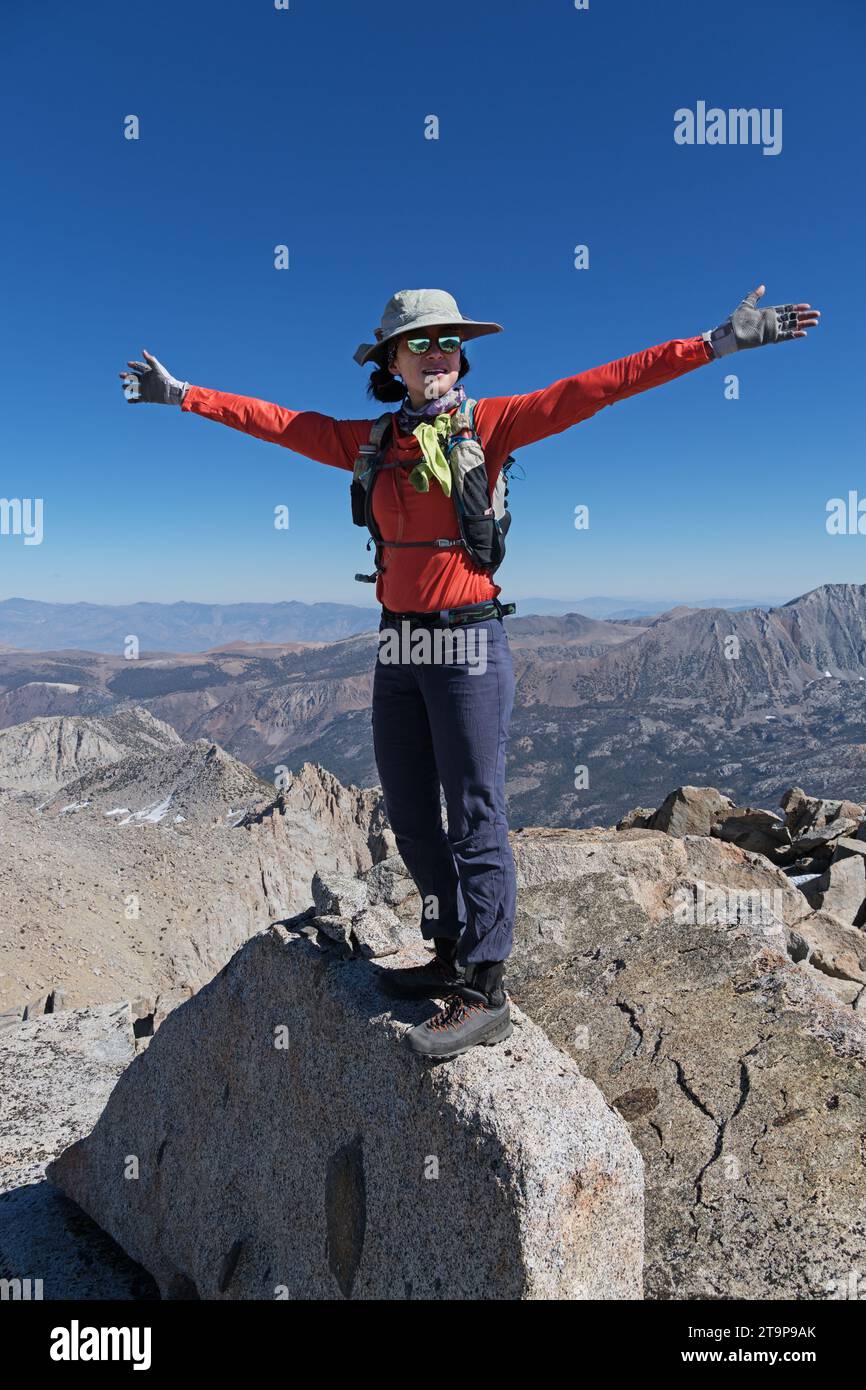 Frau auf dem Felsen auf dem Ski Mountaineers Peak in den Sierra Nevada Mountains, die mit ausgestreckten Armen feiert Stockfoto
