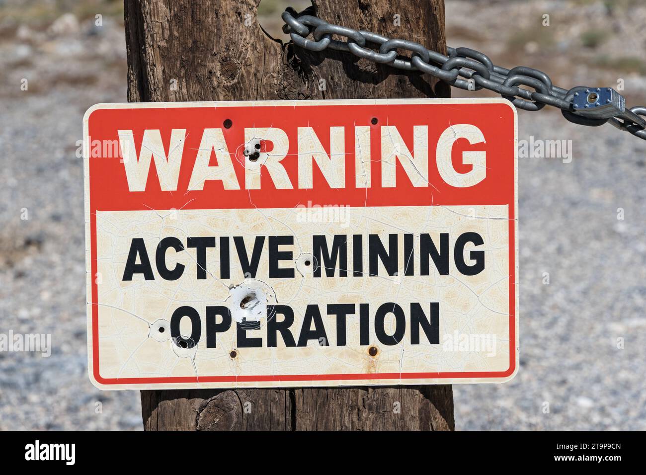 Altes rot-weiß-schwarzes Warnschild für aktiven Bergbau an einem Holzpfosten mit verriegelter Kette Stockfoto