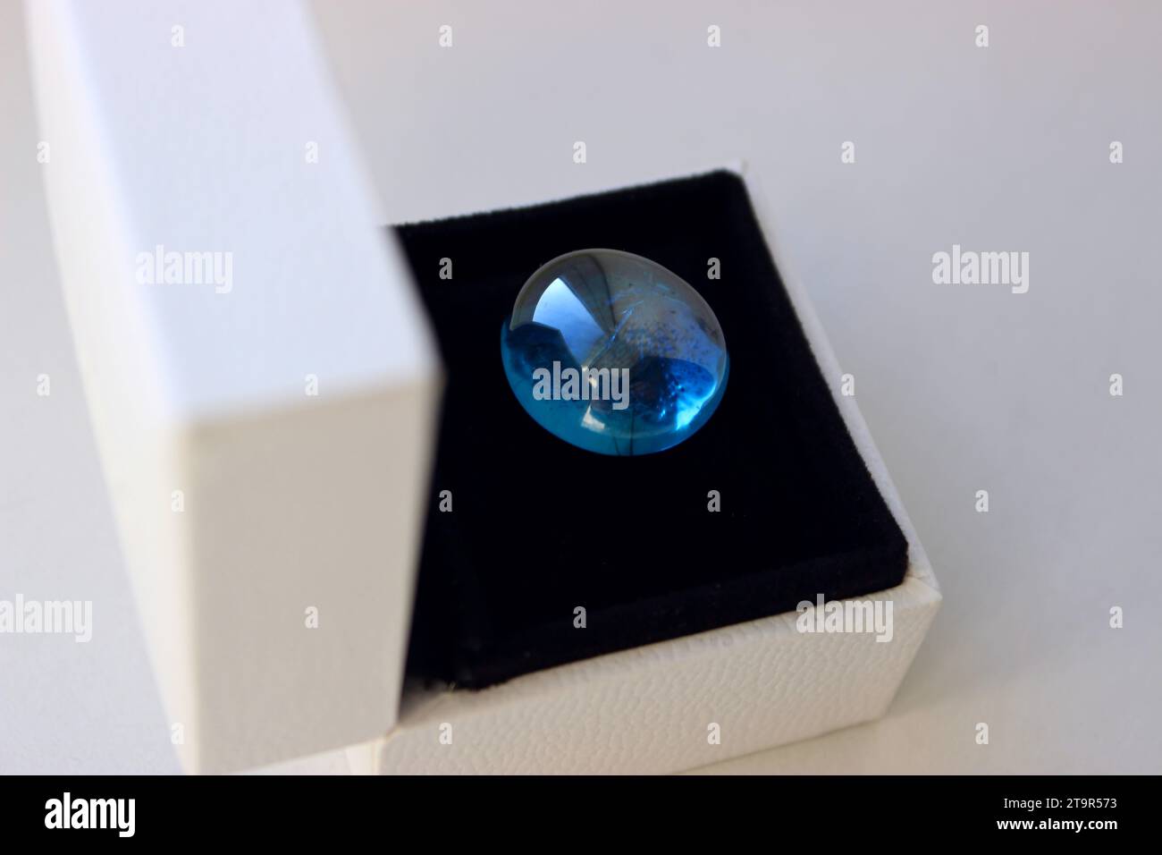 Geöffnete Schmuckschatulle mit blauem Mineralstein auf schwarzem Seidensamtpolster Stockfoto