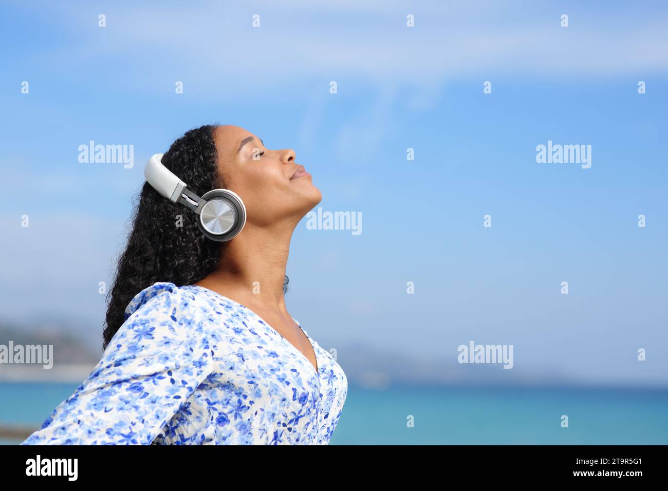 Profil einer schwarzen Frau mit Kopfhörern, Meditierende Hörführerin am Strand an einem sonnigen Sommertag Stockfoto