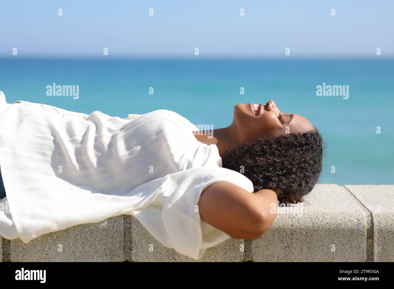 Profil einer glücklichen schwarzen Frau, die an einem sonnigen Tag am Strand liegt und ausruht Stockfoto