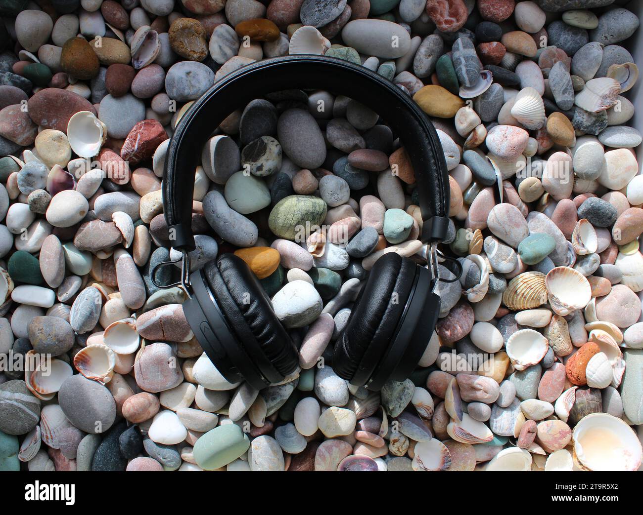 Schwarze Kopfhörer auf Einem runden farbigen Meeresstein Hintergrund als Symbol der Rockmusik Stockfoto
