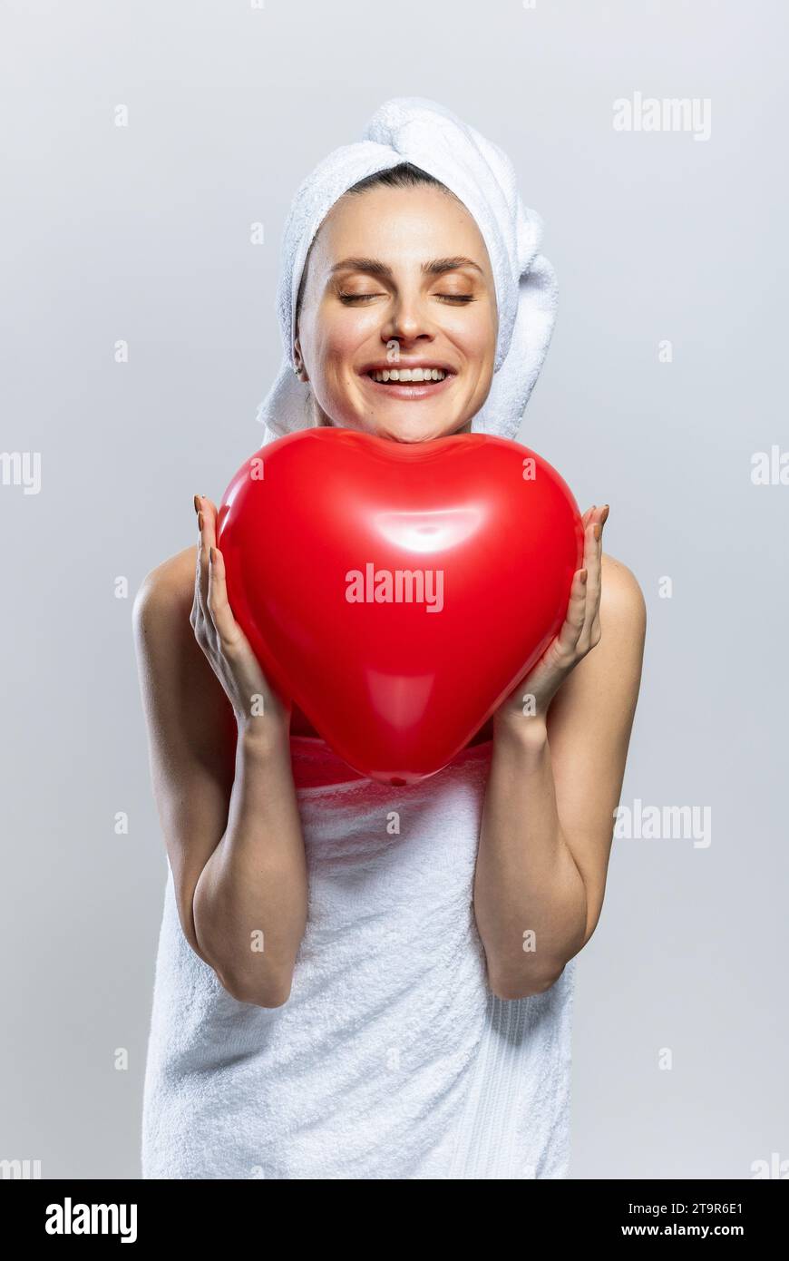 Schöne und fröhliche Frau, die weiße Handtücher trägt und ein rotes Herz hält. Valentinstag Stockfoto