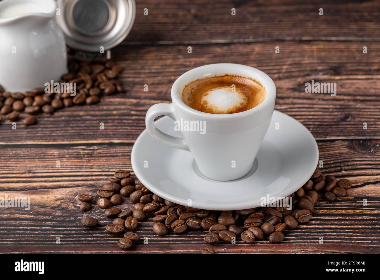 Espresso Macchiato in weißer Porzellanschale mit Milch und Kaffeebohnen auf Holztisch Stockfoto