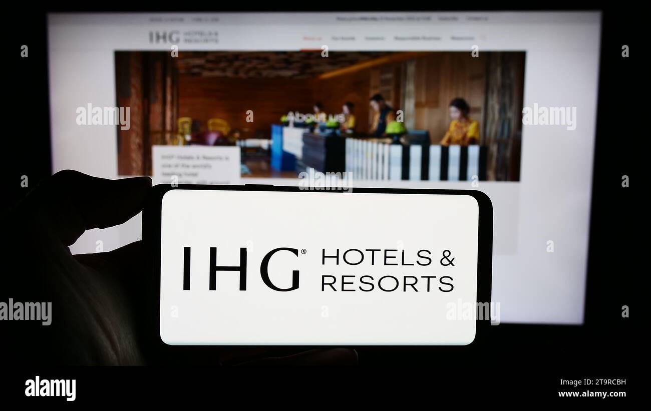 Person, die ein Mobiltelefon mit dem Logo der Hotelgesellschaft InterContinental Hotels Group plc (IHG) vor der Business-Webseite hält. Schwerpunkt auf dem Display des Telefons. Stockfoto