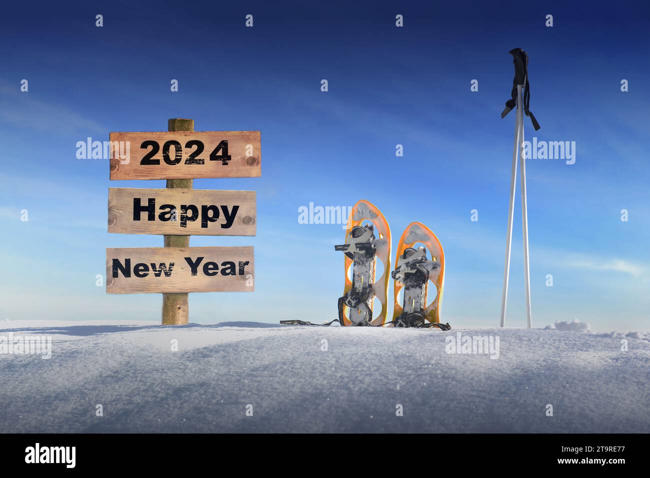 Holzschild mit Text Happy New Year 2024 im Schnee neben Schneeschuhen und Skistöcken unter blauem Himmel Stockfoto