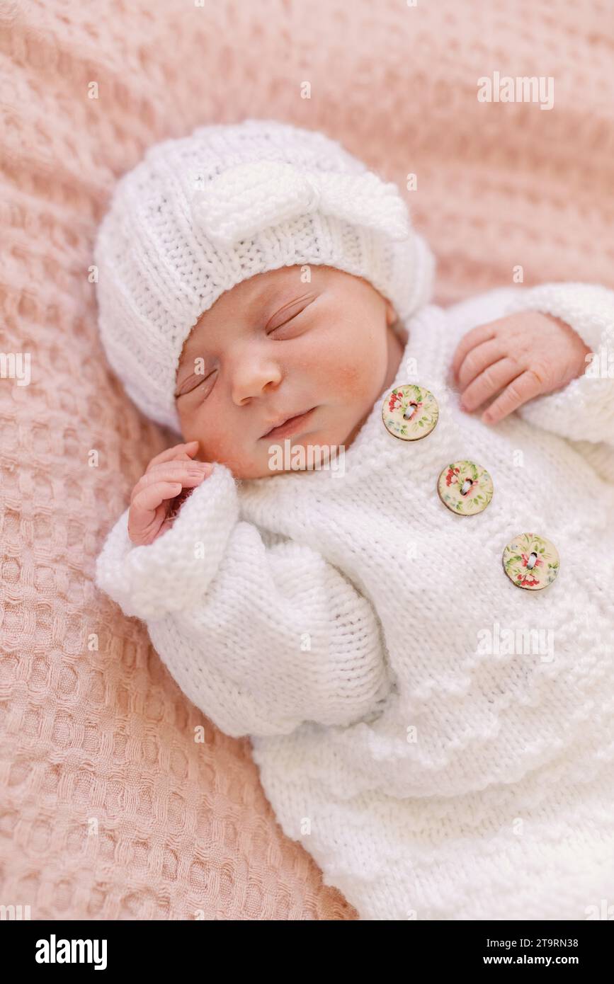 Neugeborenes Mädchen im weißen Strick-Outfit auf rosa Decke Stockfoto