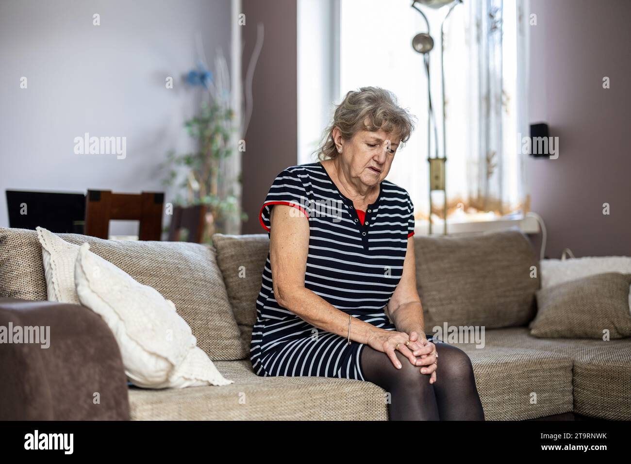 Ältere Frau, die zu Hause auf dem Sofa sitzt und an Knieschmerzen leidet Stockfoto