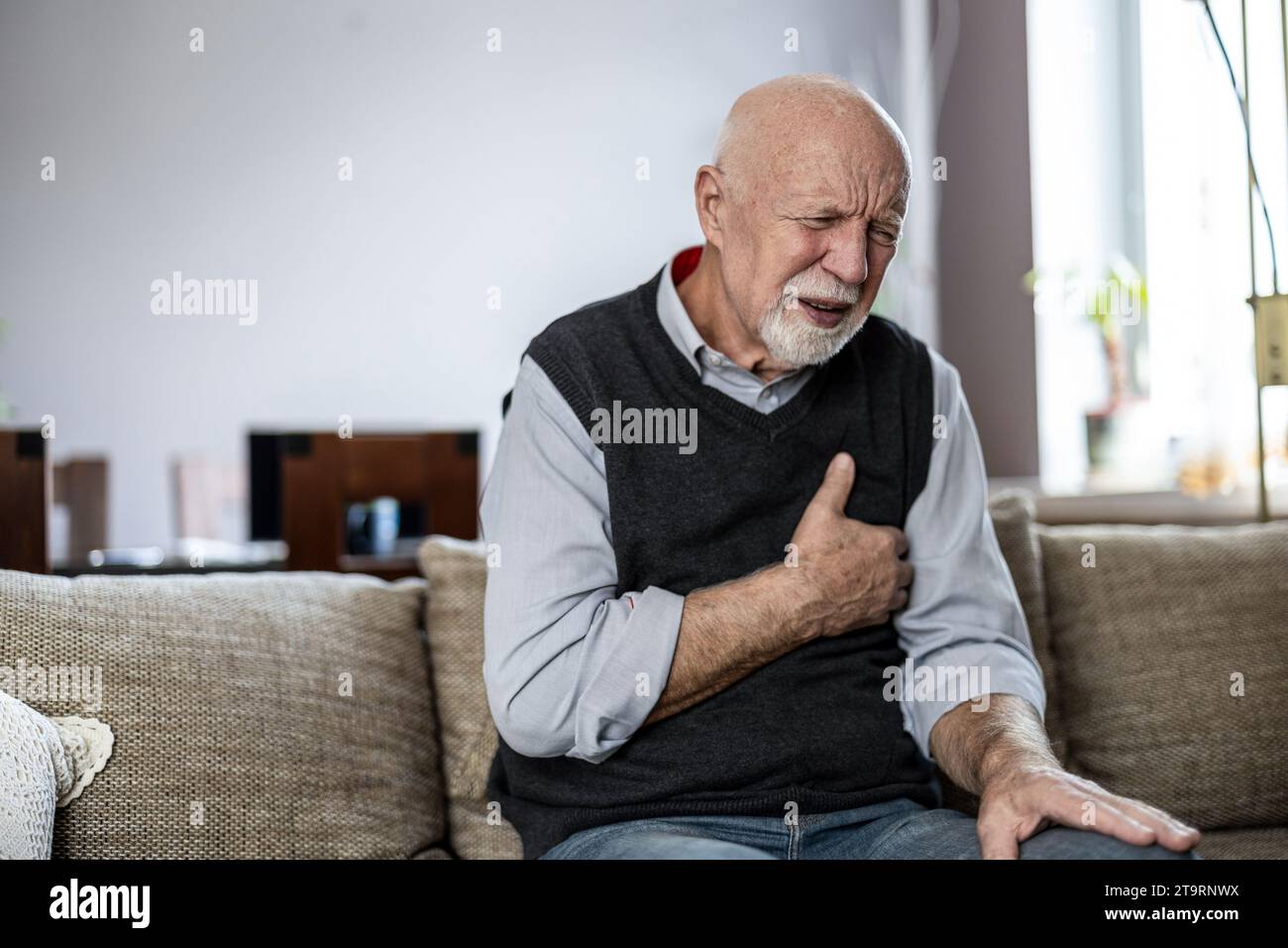 Ein älterer Mann leidet an Brustschmerzen, während er zu Hause auf dem Sofa sitzt Stockfoto