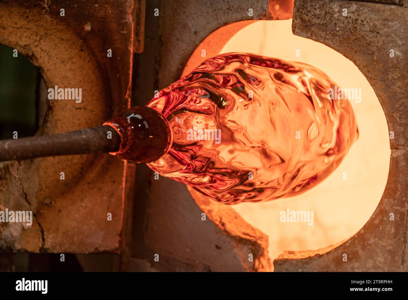 Eine große Vase aus klarem Glas wird in einem der Öfen erhitzt, die an einem 2 m langen Eisenstab befestigt sind, der Punty oder Pontil genannt wird, an der Wave Murano Glass Furna Stockfoto