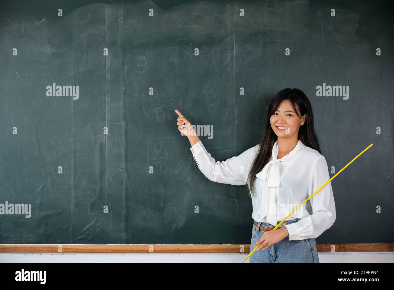 Asiatische Lehrerin lächelt mit Holzstab, der auf die Tafel zeigt Stockfoto