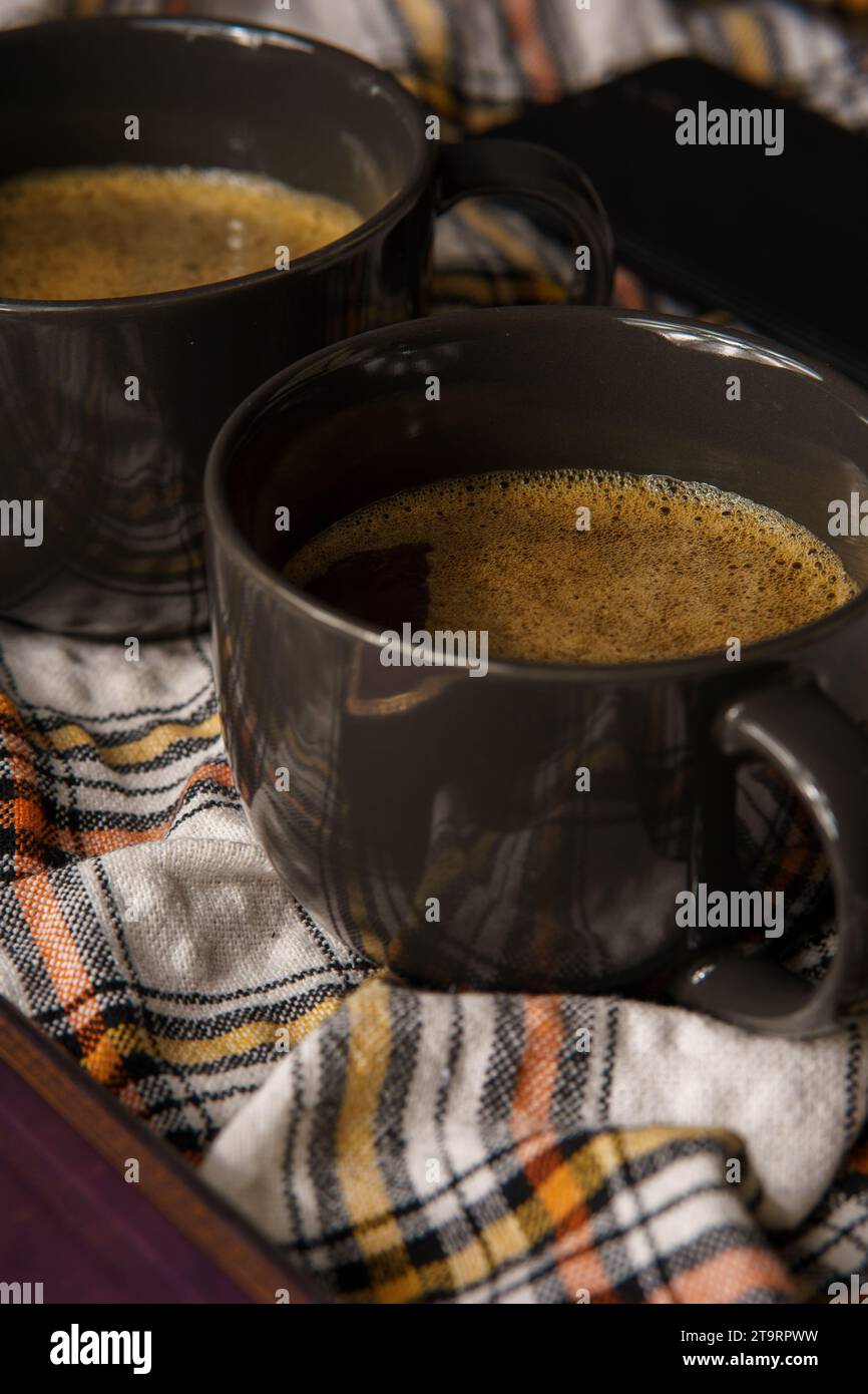 Zwei schwarze Tassen Kaffee auf einem karierten Tuch, umgeben von einem Buch und Zucker Stockfoto