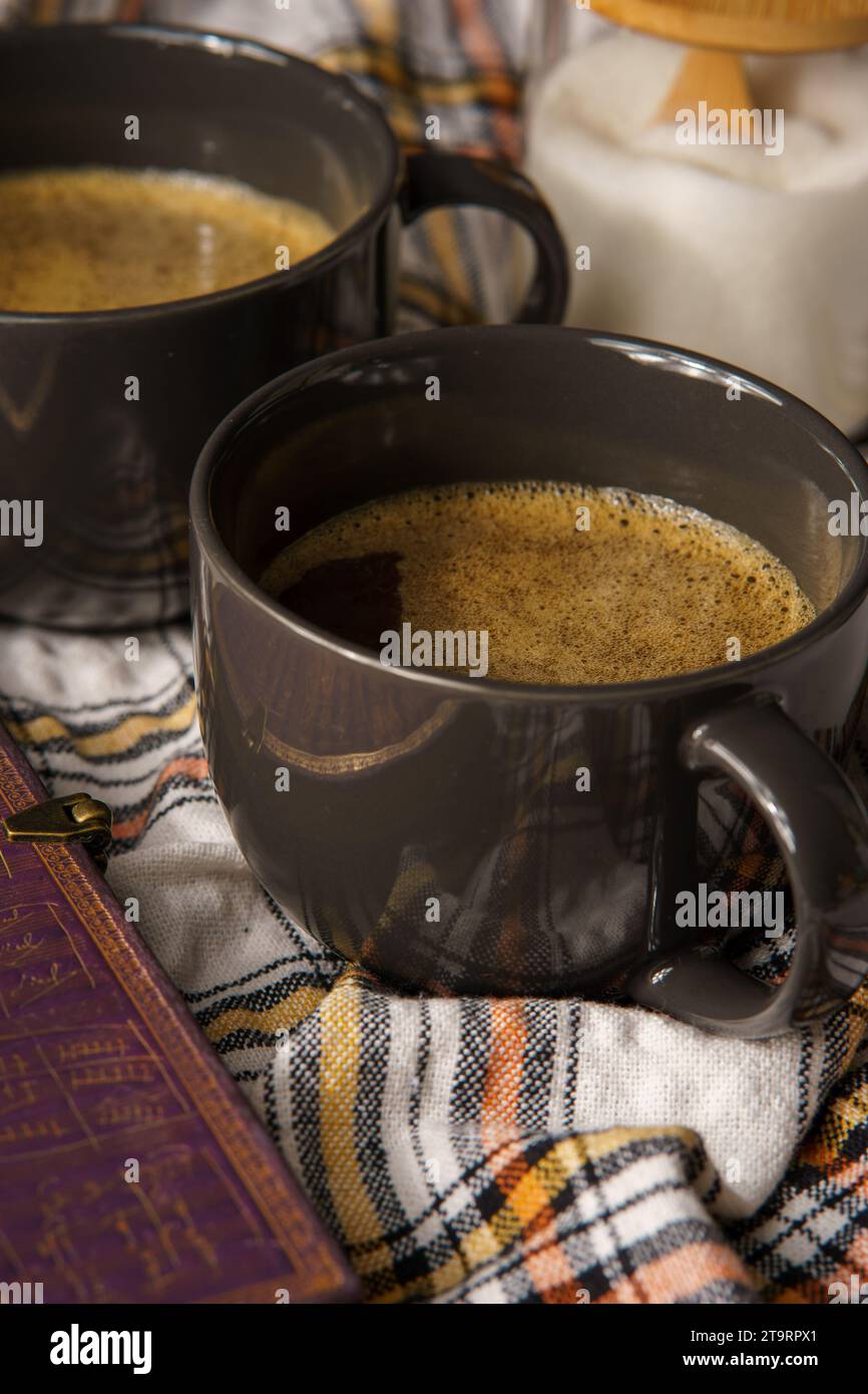 Zwei schwarze Tassen Kaffee auf einem karierten Tuch, umgeben von einem Buch und einem Smartphone. Stockfoto