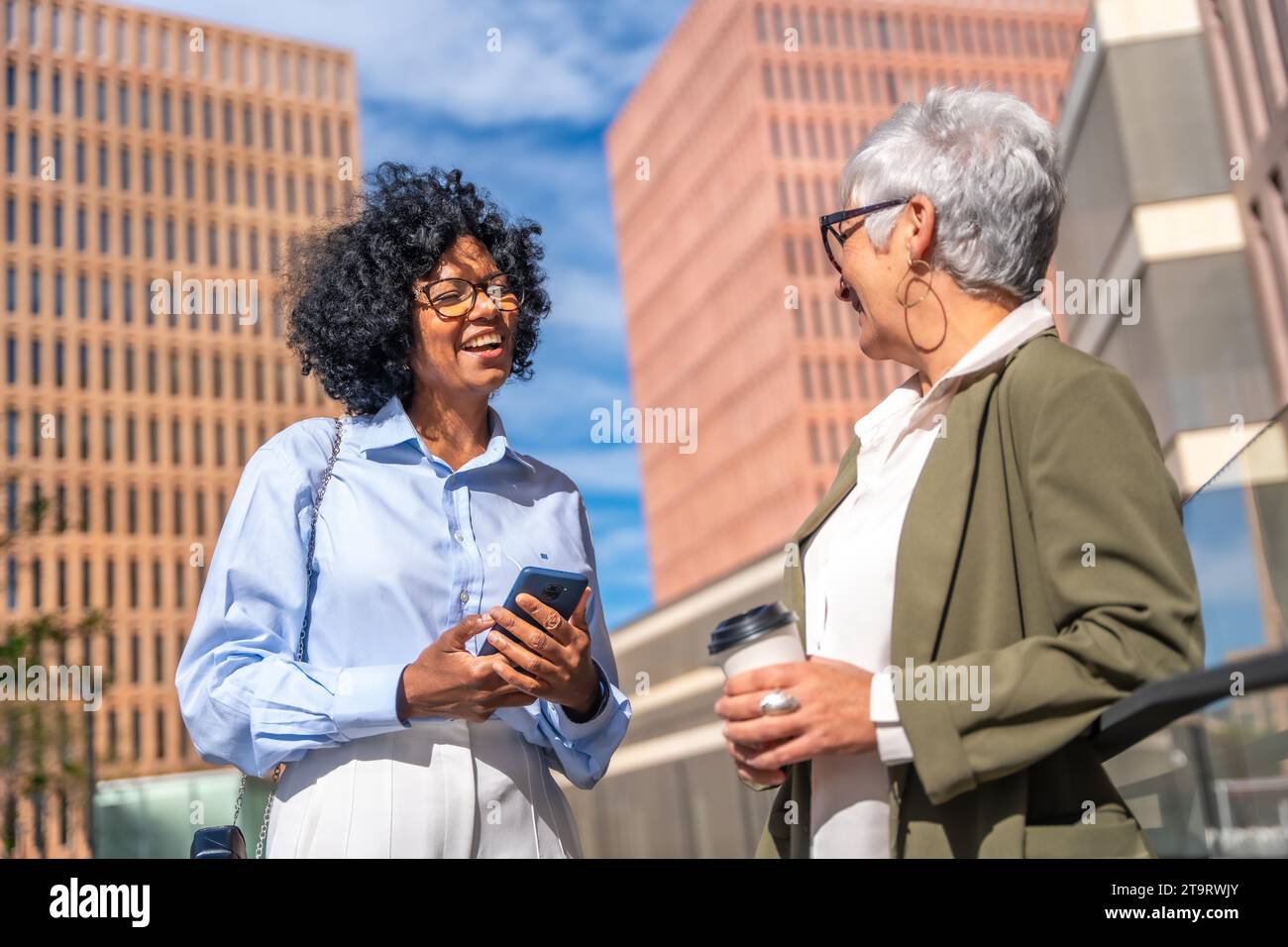 Geschäftsfrau verschiedener Generationen und ethnischer Herkunft, die sich während einer Kaffeepause im Freien entspannt unterhalten Stockfoto