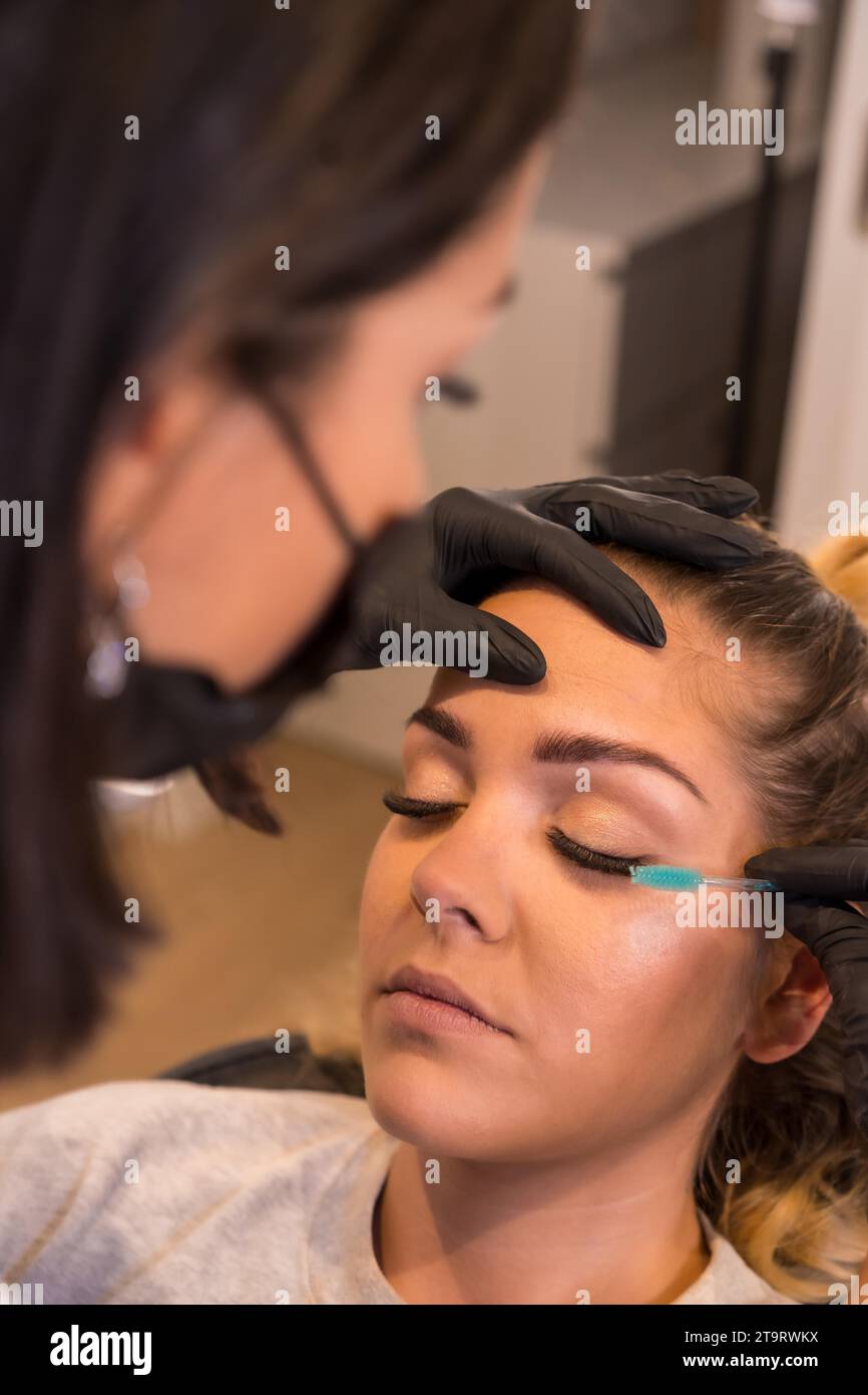 Vertikales Foto eines Profis, der Mascara auf die Wimpern der schönen Frau im Schönheitssalon aufträgt Stockfoto