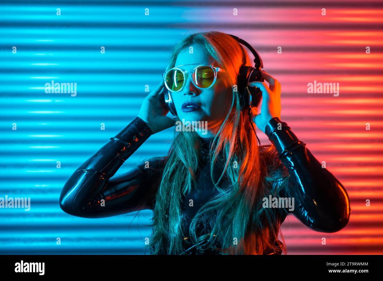 Konzentrierte Frau, die nachts in einem urbanen Raum mit geschlossenen Augen Musik hört Stockfoto
